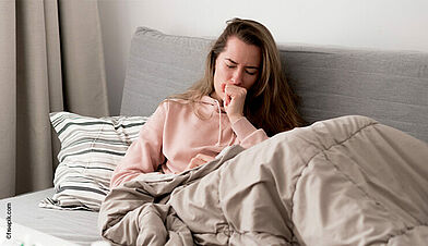 Female coughs, blanket over her legs, sitting on couch